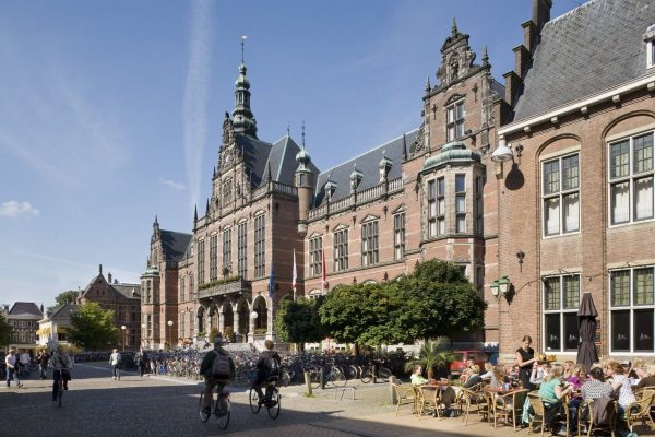 Overzicht_van_de_voorgevel_met_ingangspartij_en_bordestrap,_fietsers,_fietsenstalling_en_drukbezet_terras_op_de_voorgrond_-_Groningen_-_20416142_-_RCE